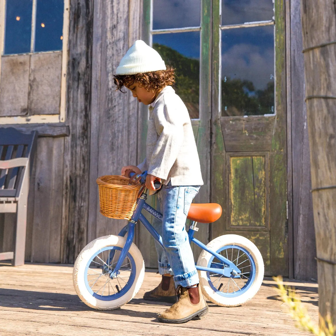 Child riding blue balance bike outdoors wearing white beanie and top