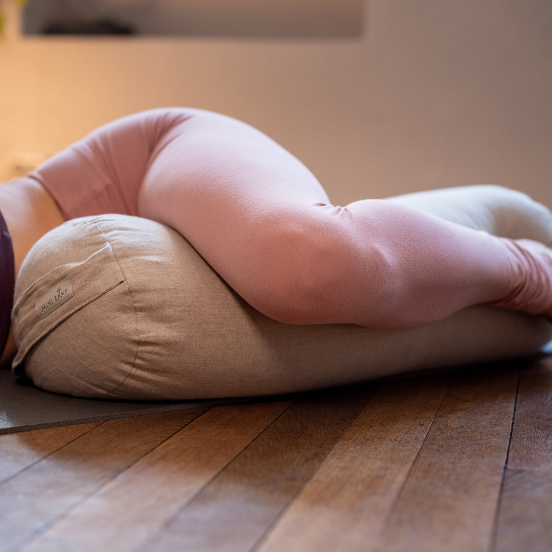 Close-up of legs resting against a MINICAMP Natural Color linen yoga bolster during a restorative stretch