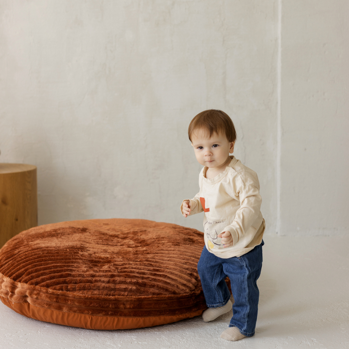 Toddler standing beside the MINICAMP terracotta corduroy floor cushion