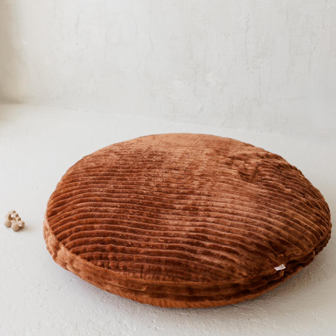 The MINICAMP terracotta corduroy floor cushion on a plain floor, showing its round shape and wide wale texture
