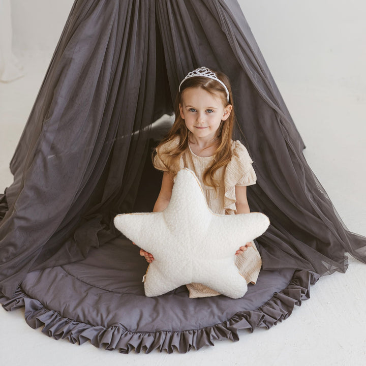 Child in a play teepee holding an ecru bouclé starfish cushion