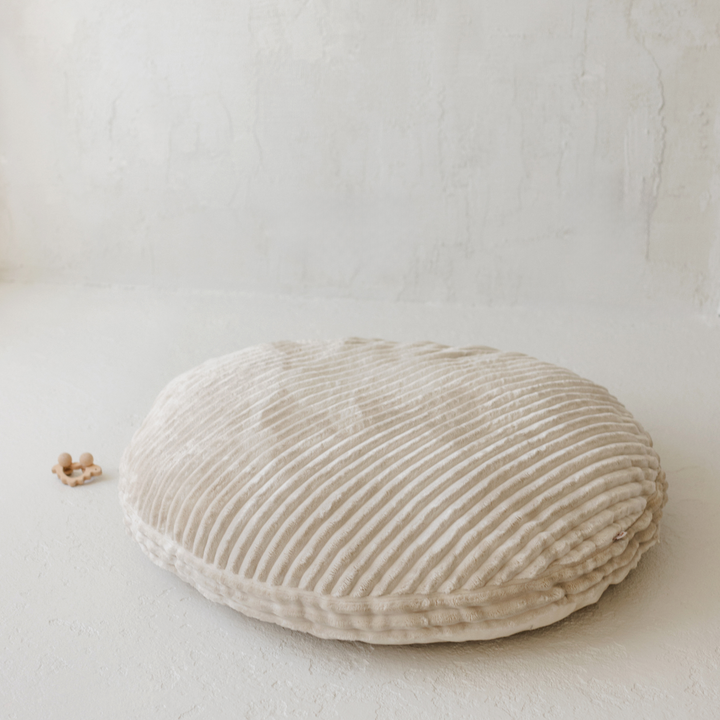 The MINICAMP ecru corduroy floor cushion on a plain floor, showing its round shape and ribbed texture