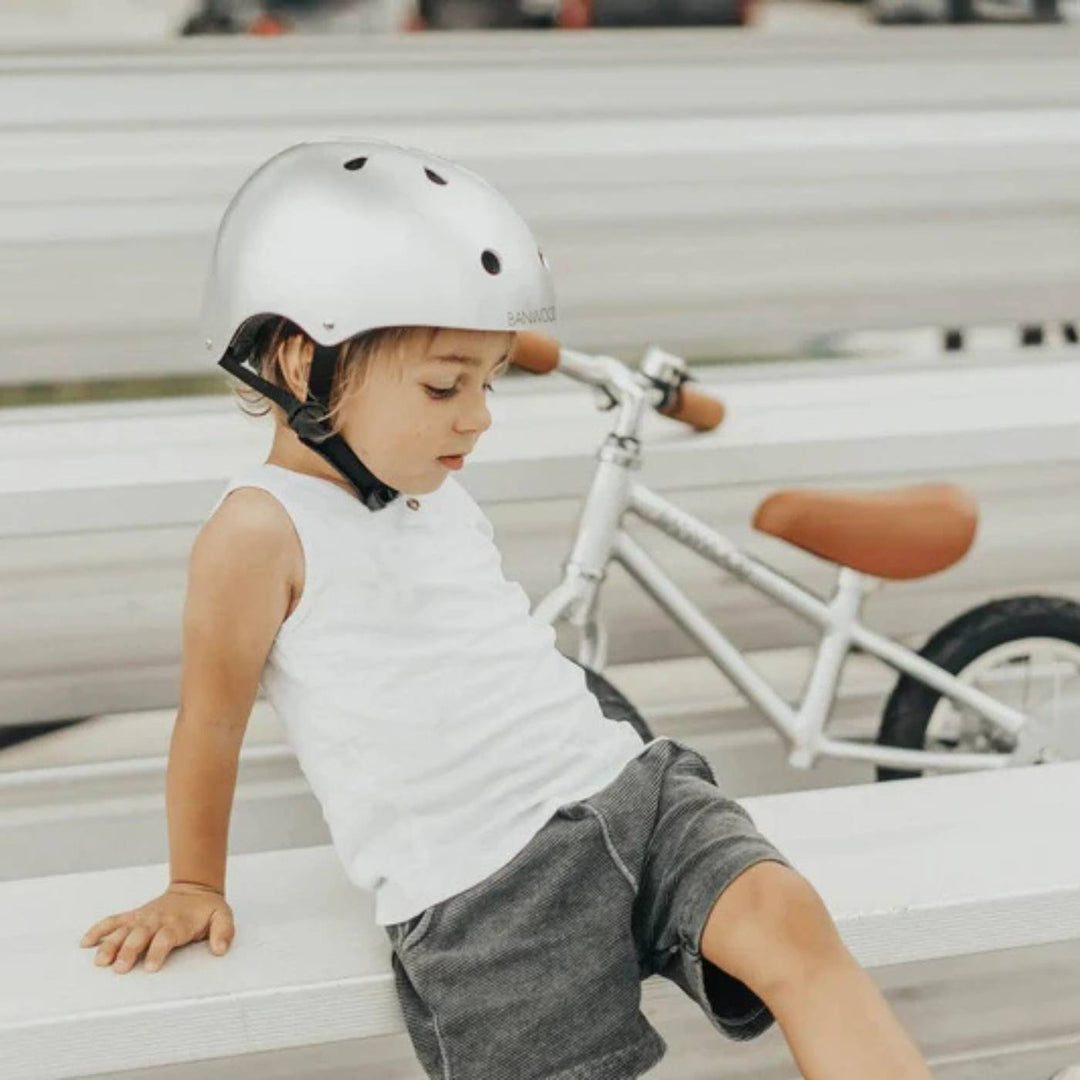 Child wearing silver Banwood helmet on white bike in outdoor lifestyle setting