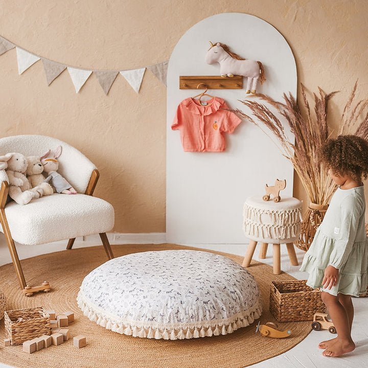 Child standing beside the MINICAMP forest animal print floor cushion in a decorated playroom