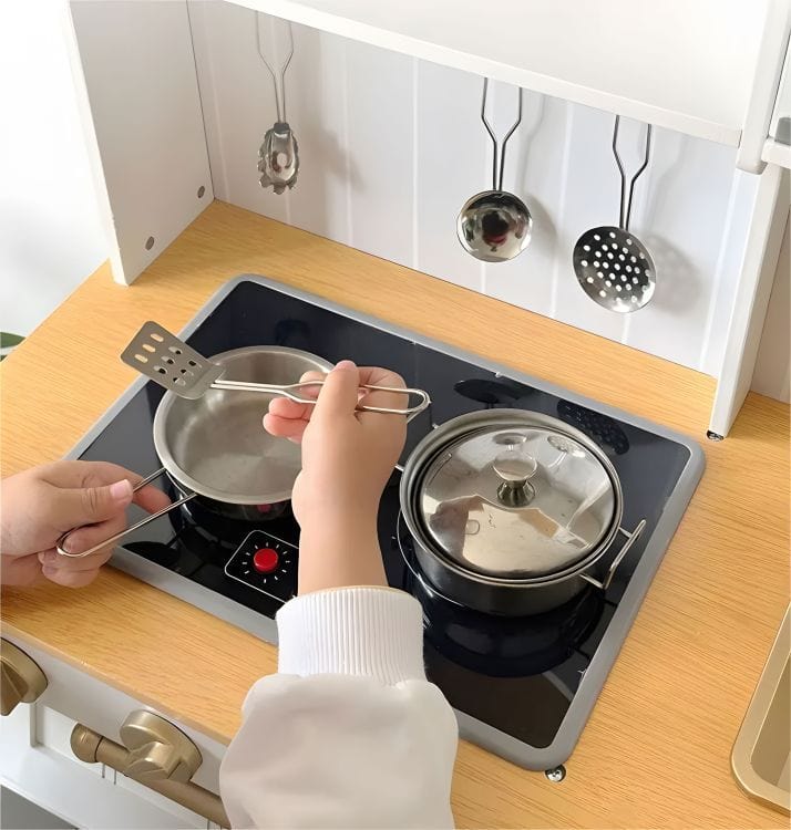 A child cooking with a spatula and tongs at the MeowBaby White &amp; Rose Gold Wooden Play Kitchen hob