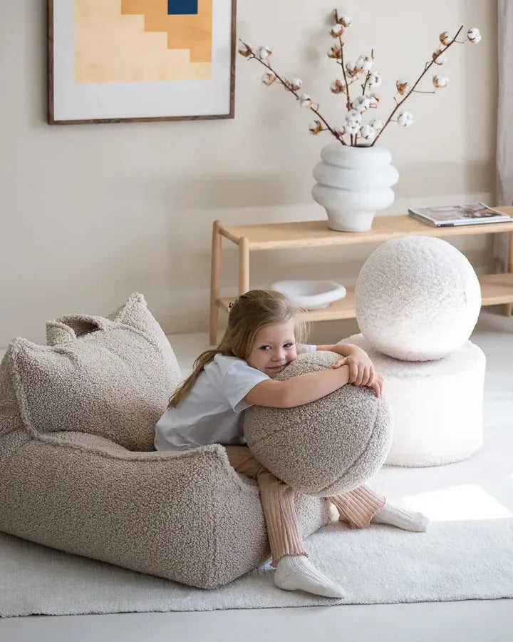 Young girl hugging a round textured cushion beside a Wigiwama bean bag in a calm living room