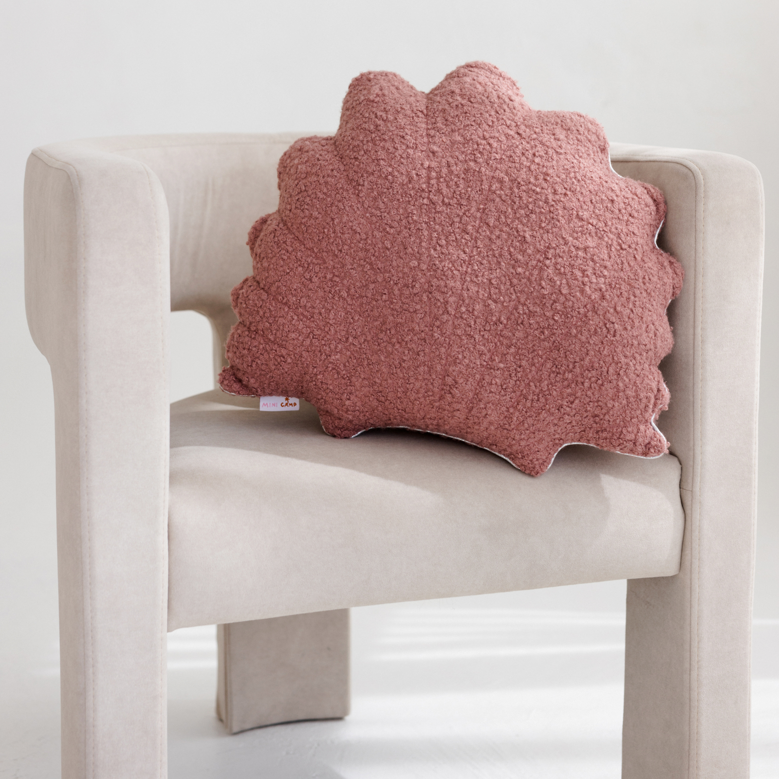 Dusty rose seashell cushion styled on a wicker chair with cream cushions